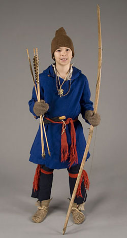 model wearing blue over-shirt, brown knit cap and mittens, holding bow and arrows.