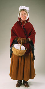 model wearing red woolen cape and striped mittens carrying small round basket