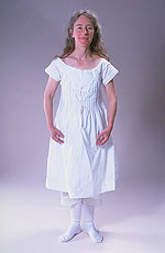 model wearing long white linen shift, lace-edged drawers and white knit stockings