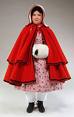 girl wearing a white quilted hood, a bright red woolen two-tiered cloak trimmed with black and a white fur muff.